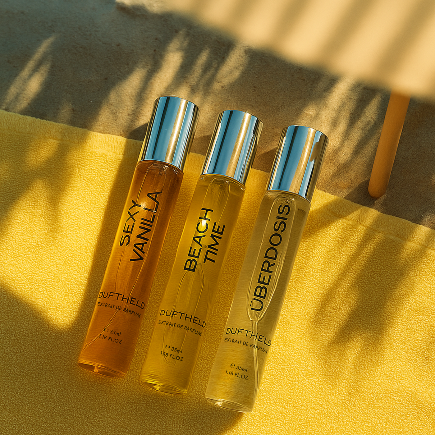 Drei Duftheld Extrait de Parfum 35-ml-Flacons mit silbernem Deckel – Sexy Vanilla, Beach Time und Überdosis – liegend auf gelbem Handtuch im Sonnenlicht.