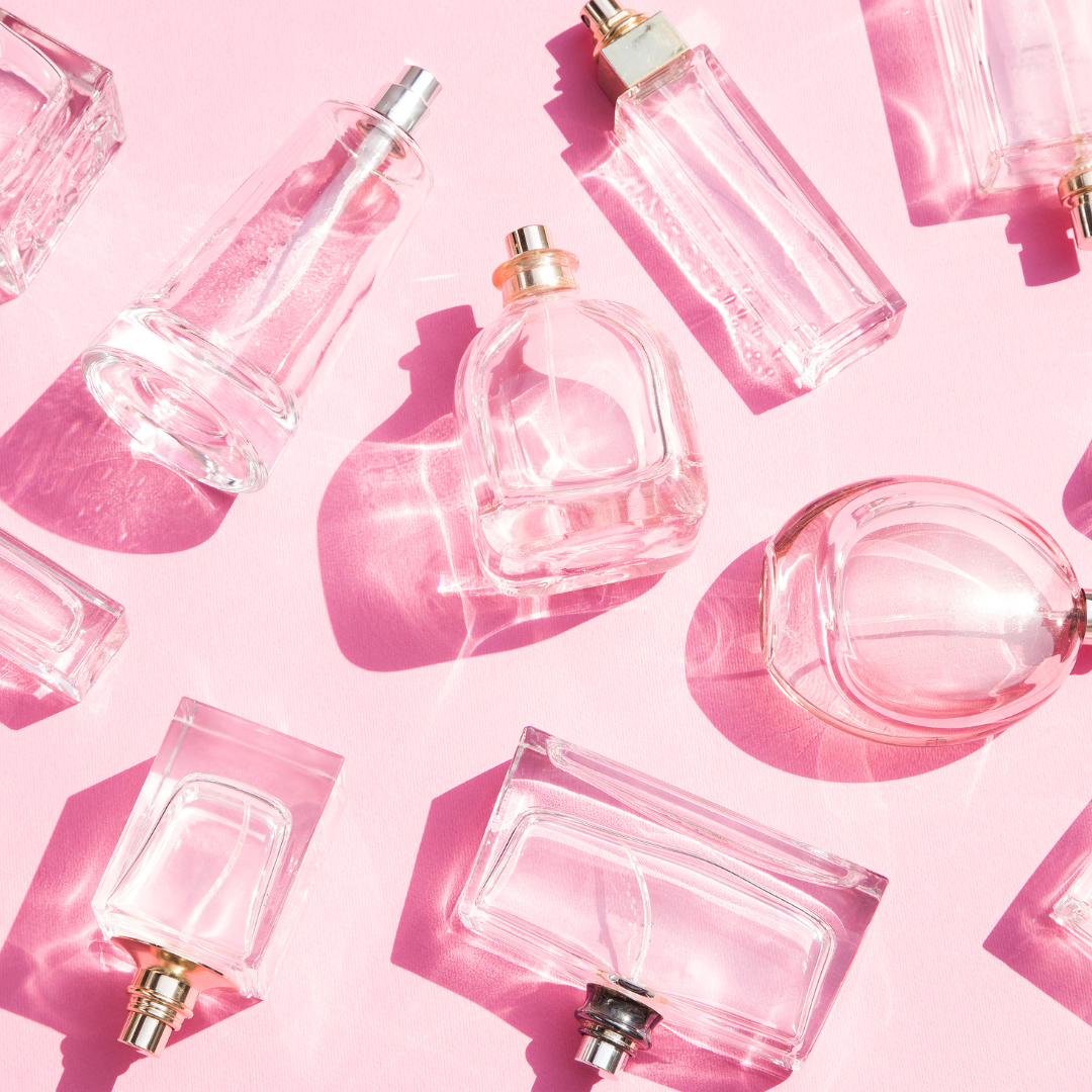 Mehrere leere, durchsichtige Parfumflakons in verschiedenen Formen liegen auf einem rosa Hintergrund, Lichtreflexe werfen glänzende Muster.